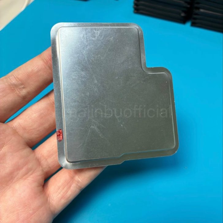 A person holding a metal heat sink or electronic component over a blue surface.