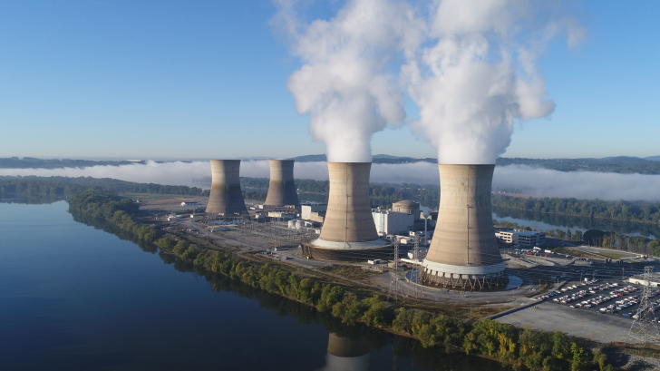 Nuclear power plant with cooling towers and steam emissions by a river.