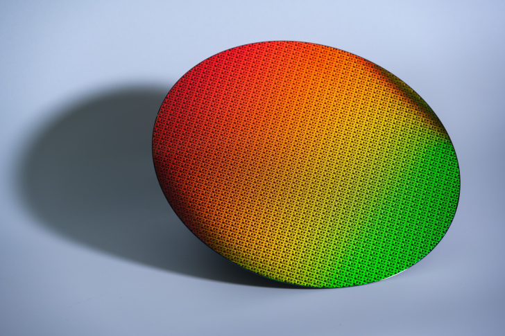 Colorful semiconductor wafer with intricate patterns, reflecting red to green gradient light.