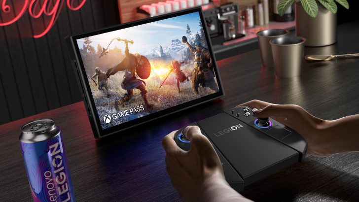Lenovo Legion controller held by hands next to a tablet displaying Game Pass and a can labeled Lenovo Legion on a table.