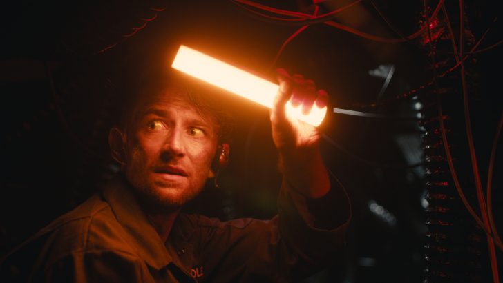 Person holding an unbranded orange light in a dimly lit area with visible wires.