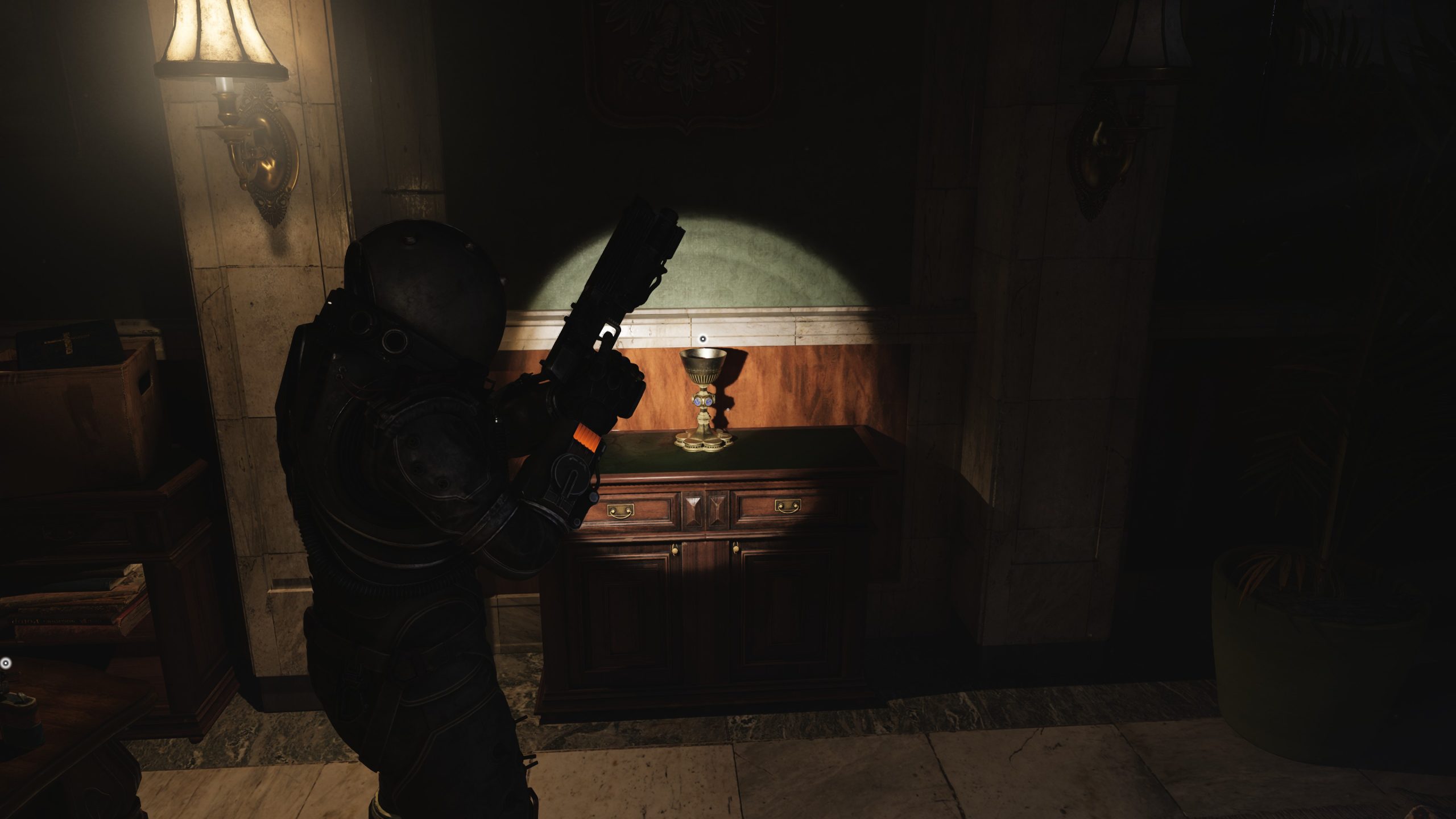 Person in black armor holding a large weapon stands in a dimly lit room next to a wooden cabinet.
