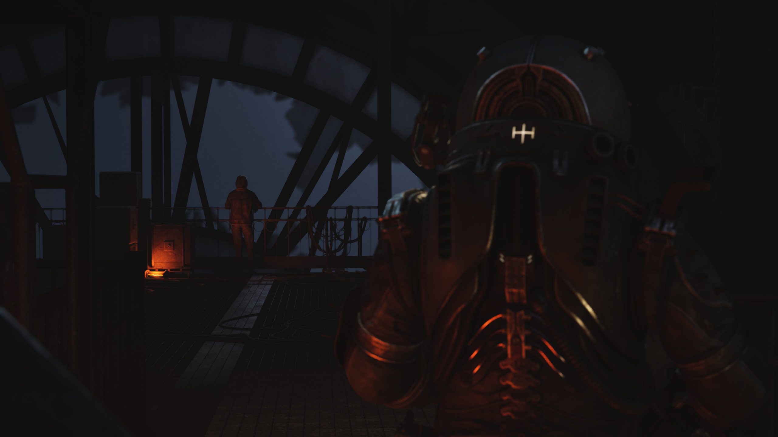 A figure in a dark suit with a helmet featuring the letter H is inside a dimly lit industrial setting.