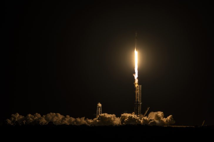 Rocket launch at night with bright exhaust flame and smoke trail visible.