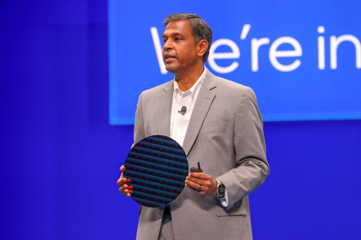 Individual holding a semiconductor wafer on stage under partial text reading We're in.