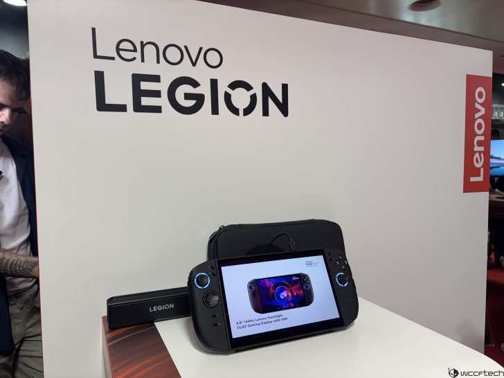 Lenovo Legion handheld gaming device displayed on a table with Lenovo PureSight Gaming Display with VRR on the screen.