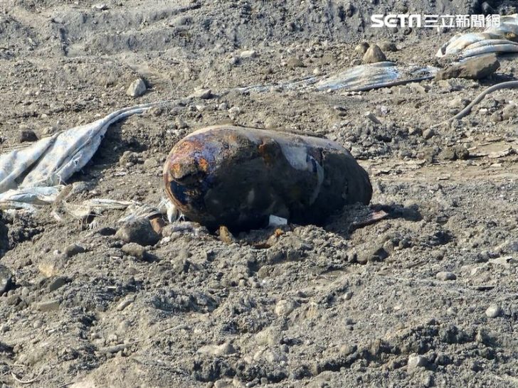Large rusted object lies on rocky ground, text SCTM in corner.