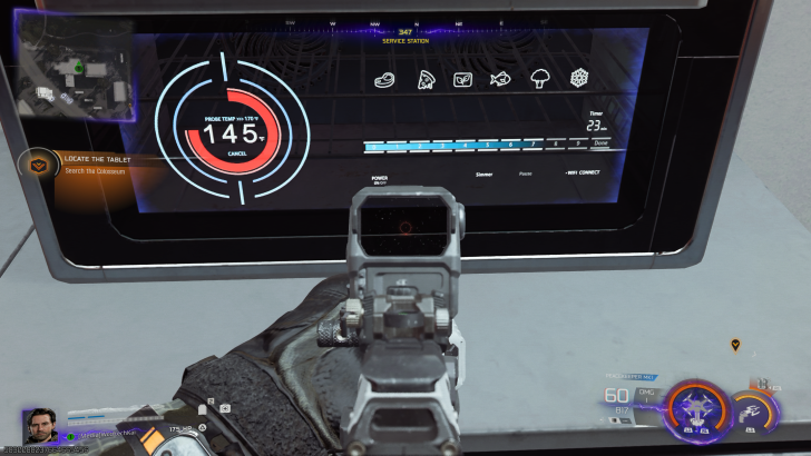 In a video game scene, a character is aiming a rifle at a digital display showing a probe temperature of '145°F' with the task 'Locate the Tablet: Search the Colosseum'.
