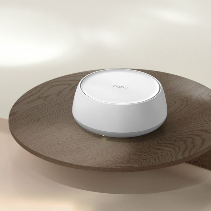 A TP-Link Deco router with a smooth, round design is placed on a wooden table in a minimalistic setting.