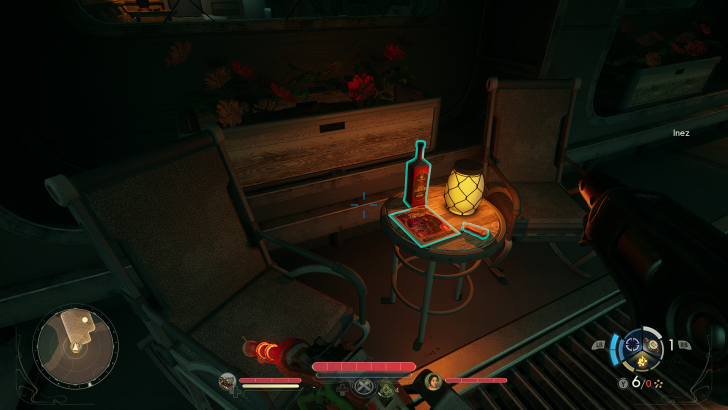 Chair and table setup next to a planter, with a bottle and a magazine on the table, in a dimly lit room labeled Inez.