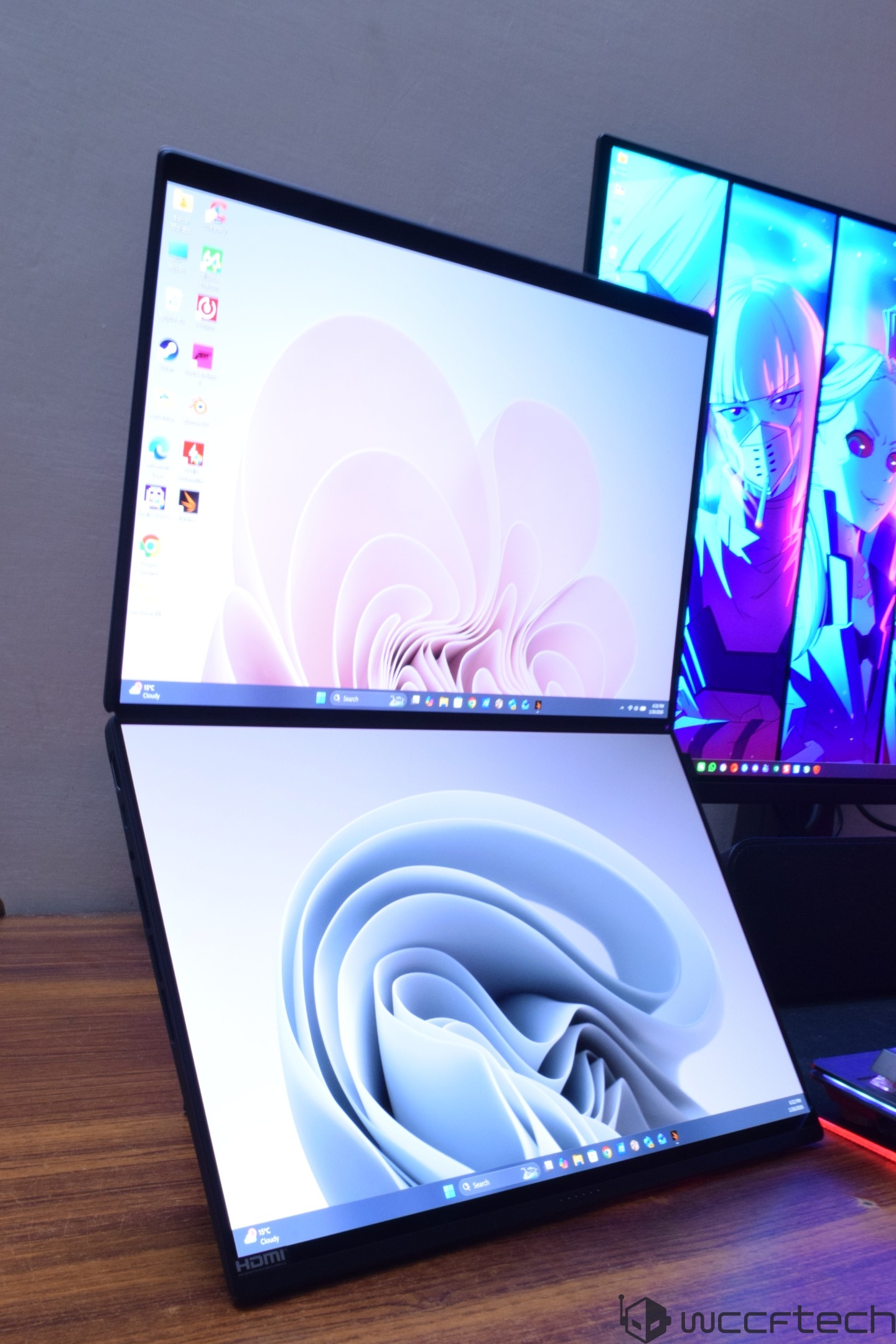 A dual-screen setup with two vertically stacked monitors, both displaying abstract light swirl wallpapers, sits on a wooden