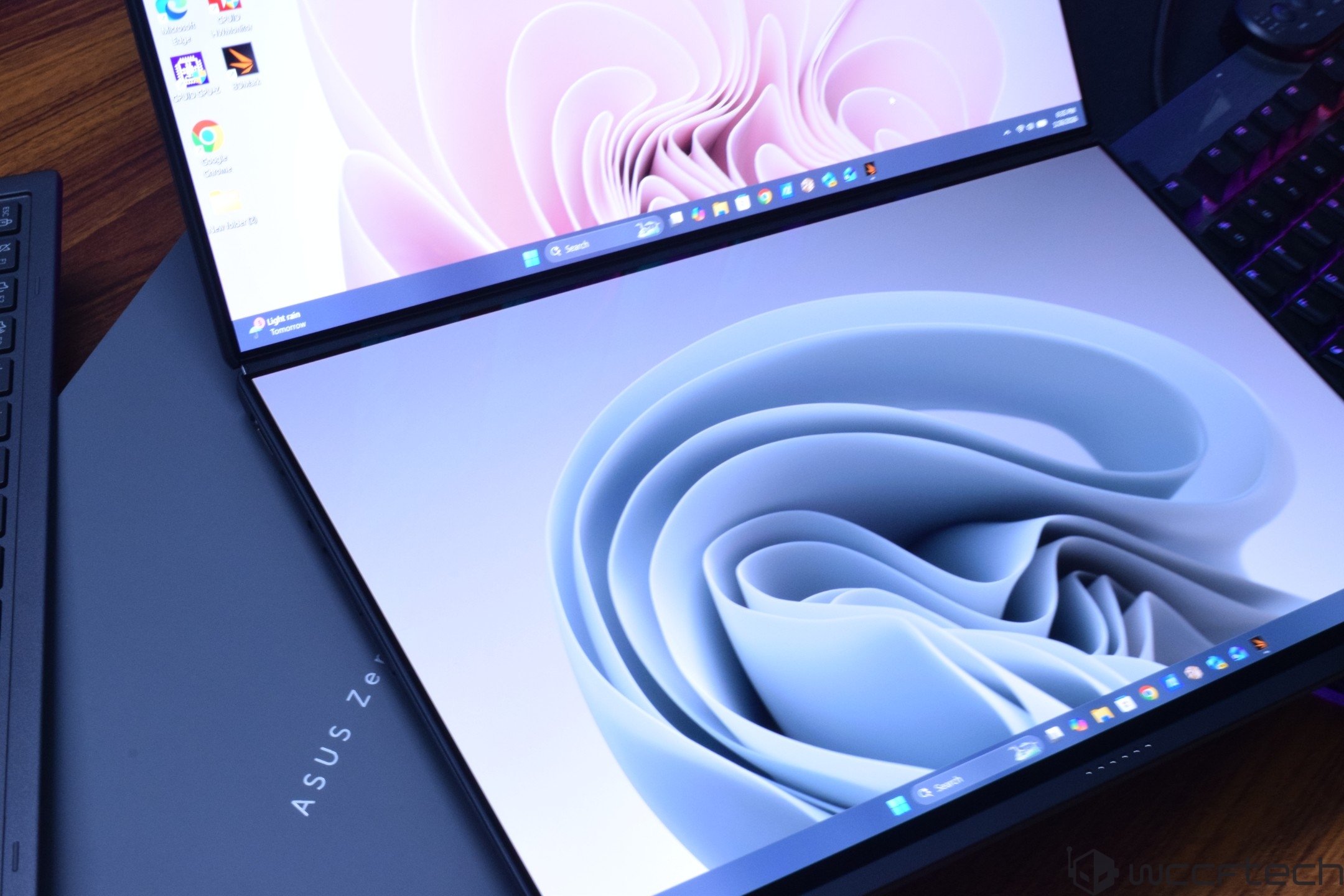 An ASUS Zenbook Fold showing a dual-screen display with abstract wallpapers on both screens.