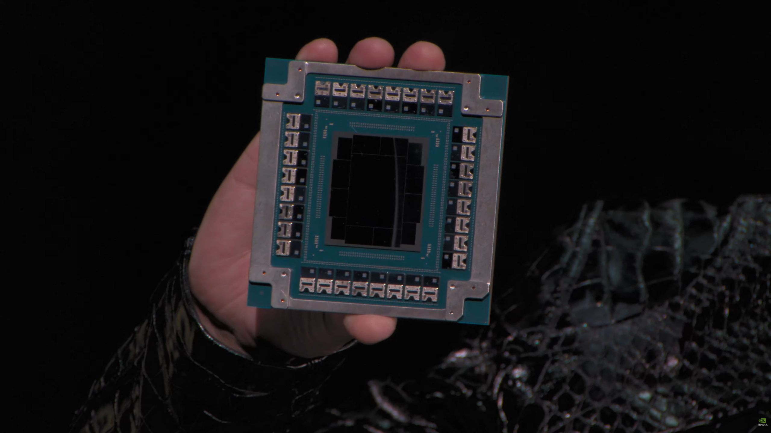 A person holds an NVIDIA compute chip with visible circuitry details against a dark background.