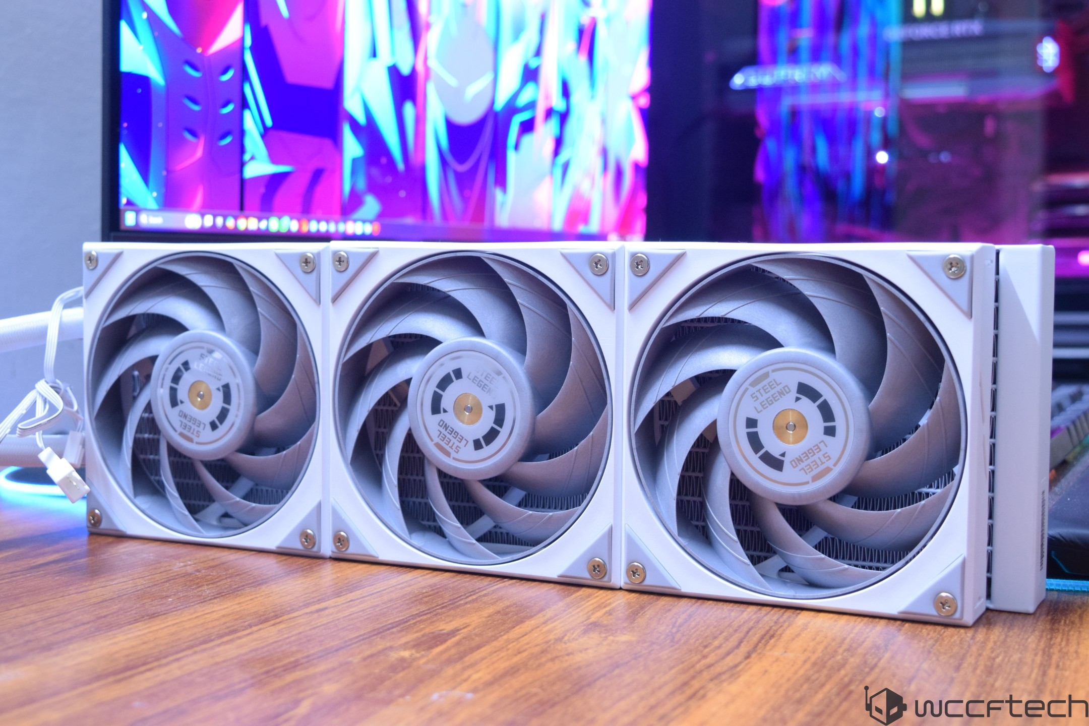 Three ASRock Steel Legend fans mounted on a white radiator in front of a colorful desktop background.