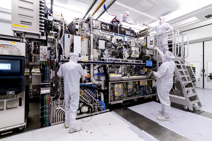 Technicians in cleanroom suits working on a large semiconductor manufacturing machine.