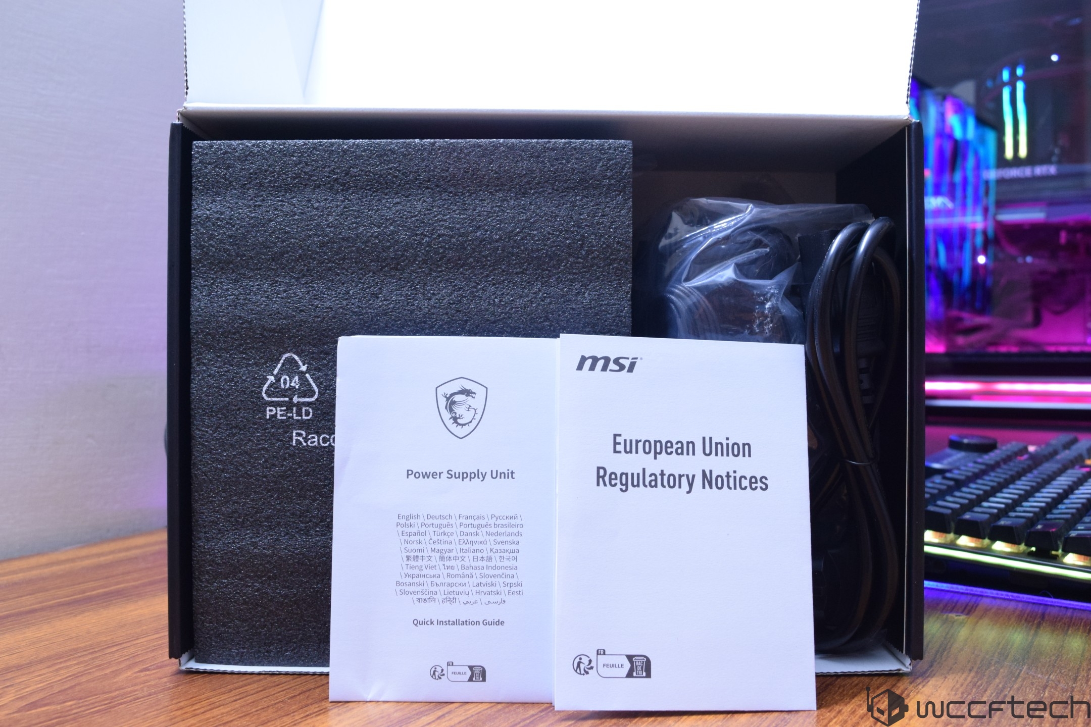 An MSI power supply unit package is opened, showing a power cable and documents titled 'Power Supply Unit Quick Installation Guide' and 'European Union Regulatory Notices.'