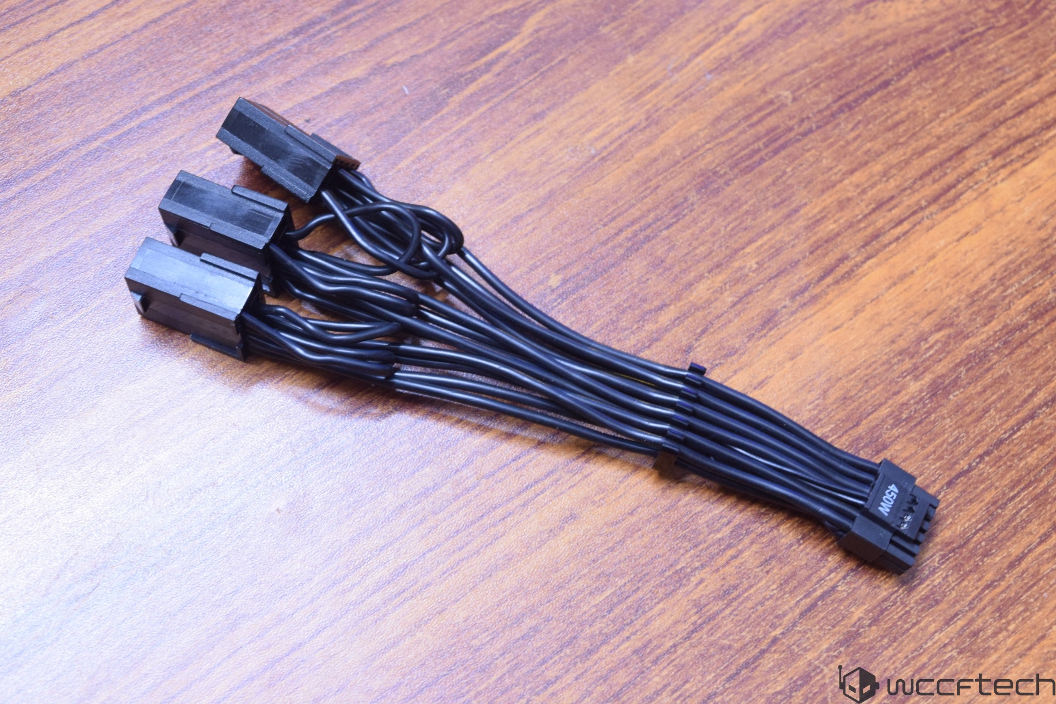 A close-up of a black 'INCS' labeled power cable splitter with multiple connectors on a wooden surface.