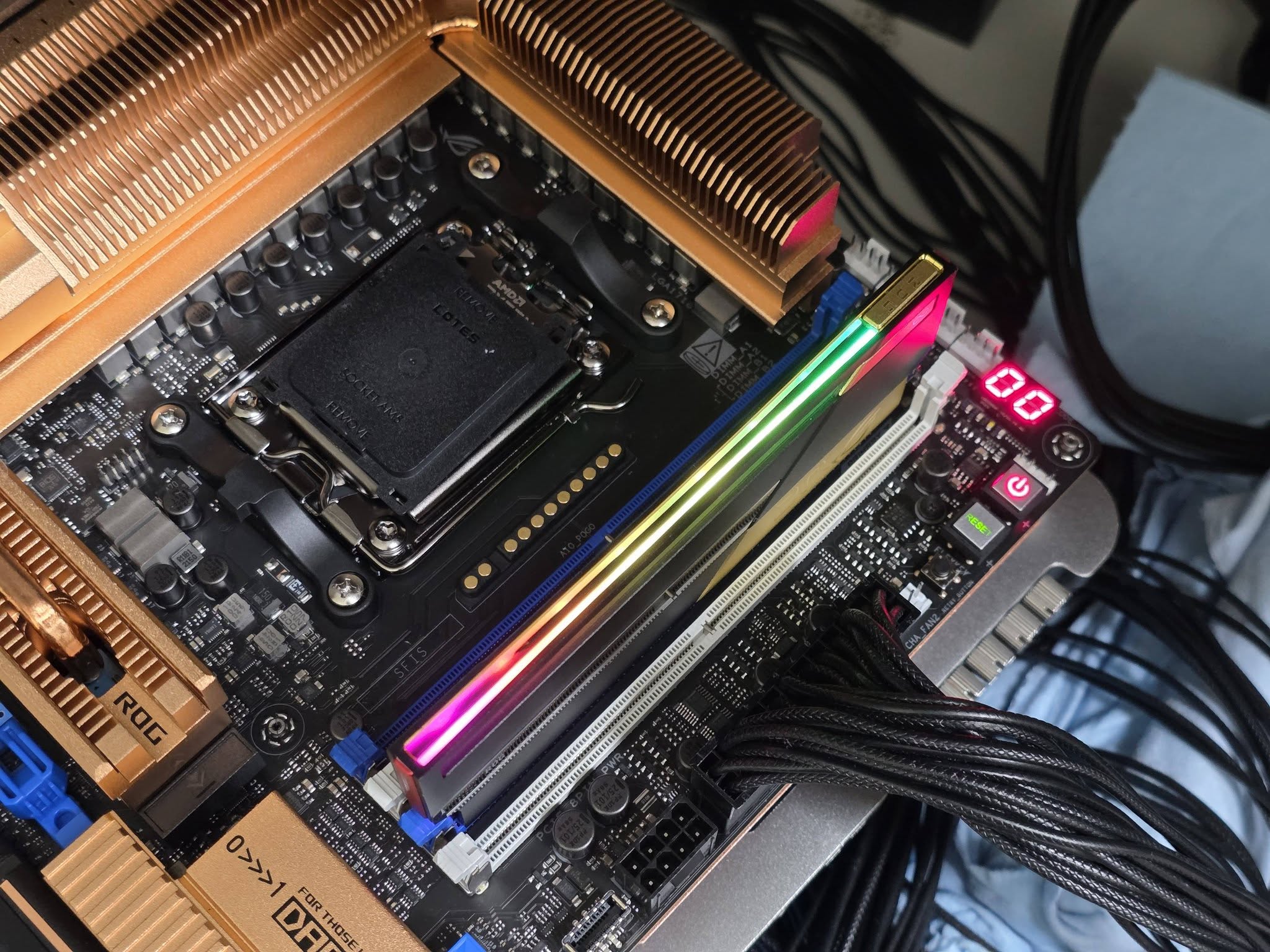 An ASUS ROG motherboard featuring a Lotes socket, RGB RAM, copper heatsinks, and a digital readout displaying '00'.