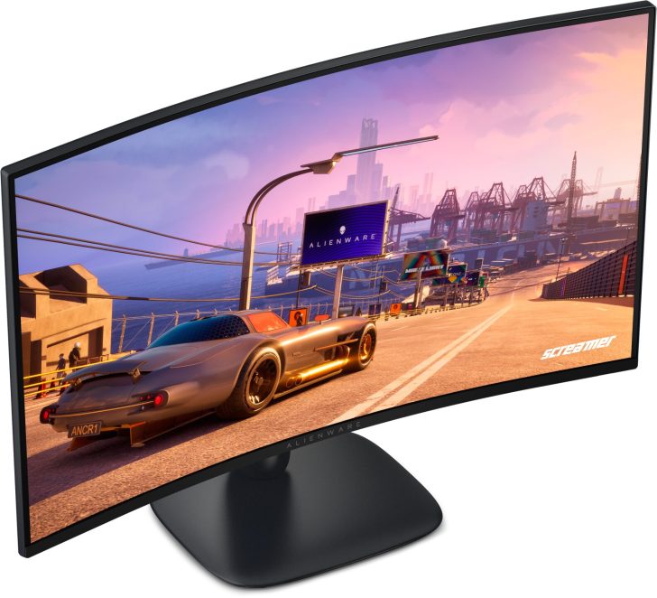 A curved Alienware monitor displays a racing game with a sports car on a sunlit highway, and the brand logo is visible on a billboard in the game.