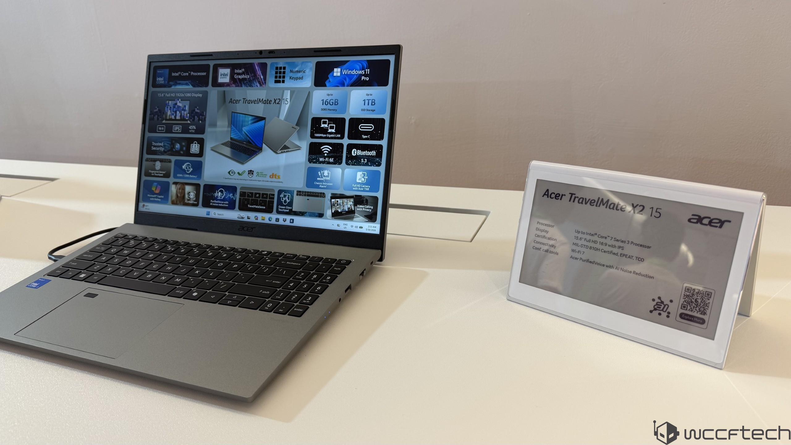 An Acer TravelMate X2 15 laptop is displayed with its specifications on-screen, including '16GB DDR5 Memory' and '1TB SSD Storage,' next to a sign highlighting its Intel Core i7 processor and other features.
