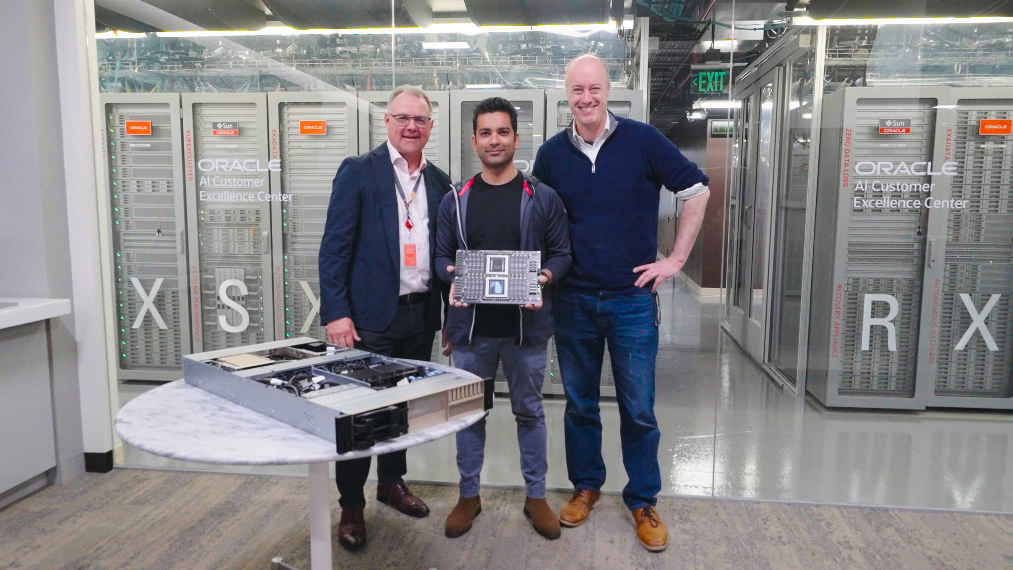 Three people stand in front of Oracle servers at the Oracle AI Customer Excellence Center, with one person holding a hardware component.