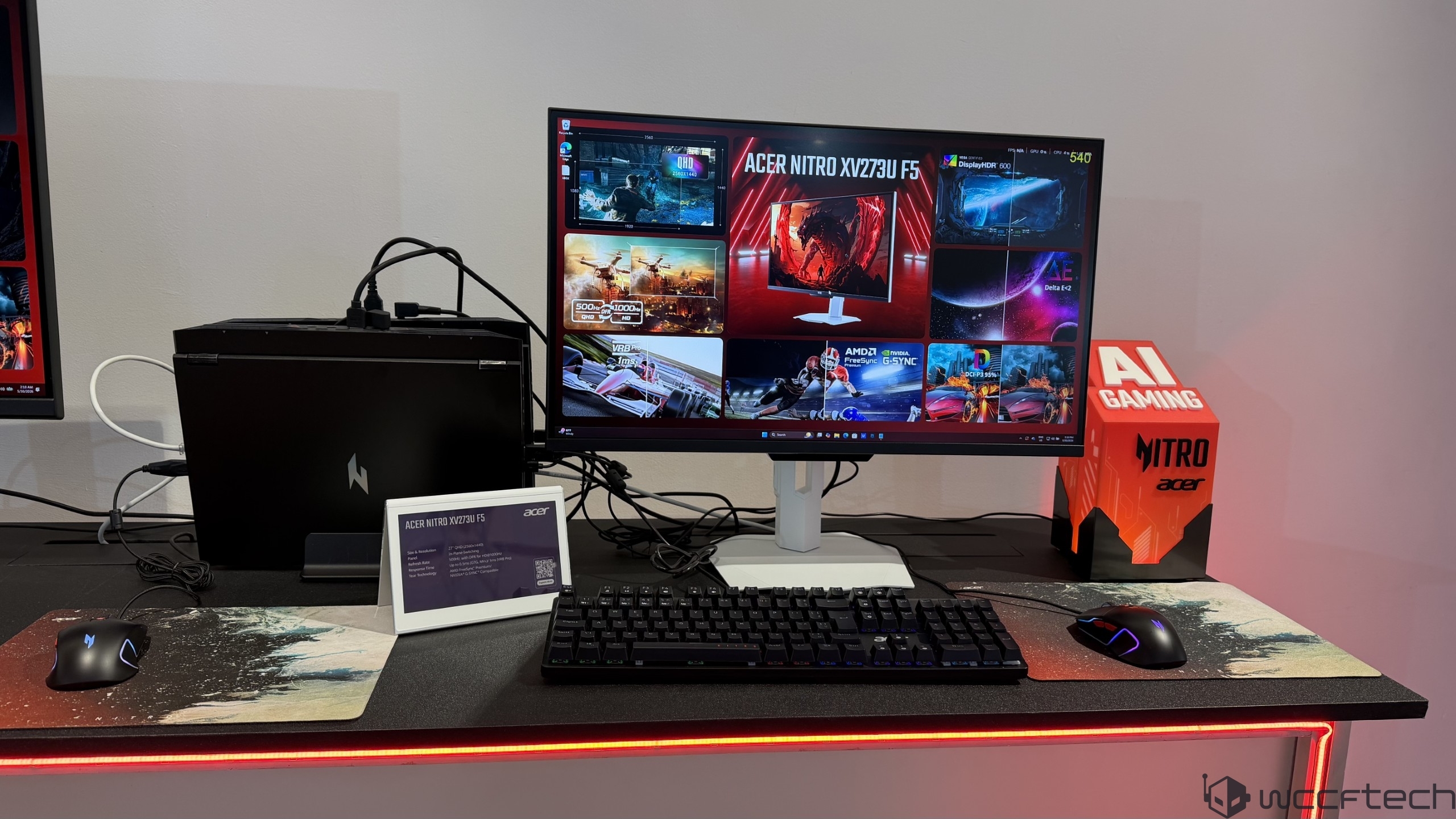 The Acer Nitro XV273U F5 gaming monitor is displayed on a desk setup along with peripherals and a sign reading AI Gaming.