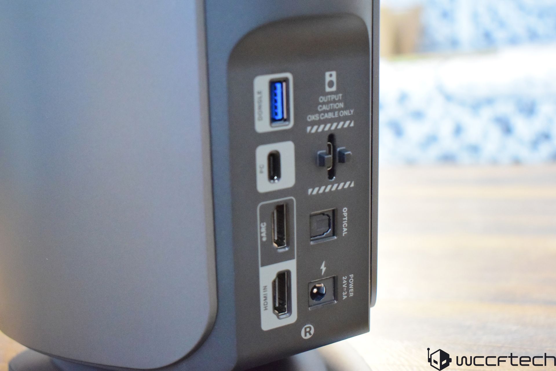 The back panel of an unbranded speaker displays various ports labeled as 'SERVICE,' 'PC,' 'HDMI IN,' 'OPTICAL,' and 'POWER 24V/3A,' along with a slider switch marked 'OUTPUT CAUTION QXS CABLE ONLY.'