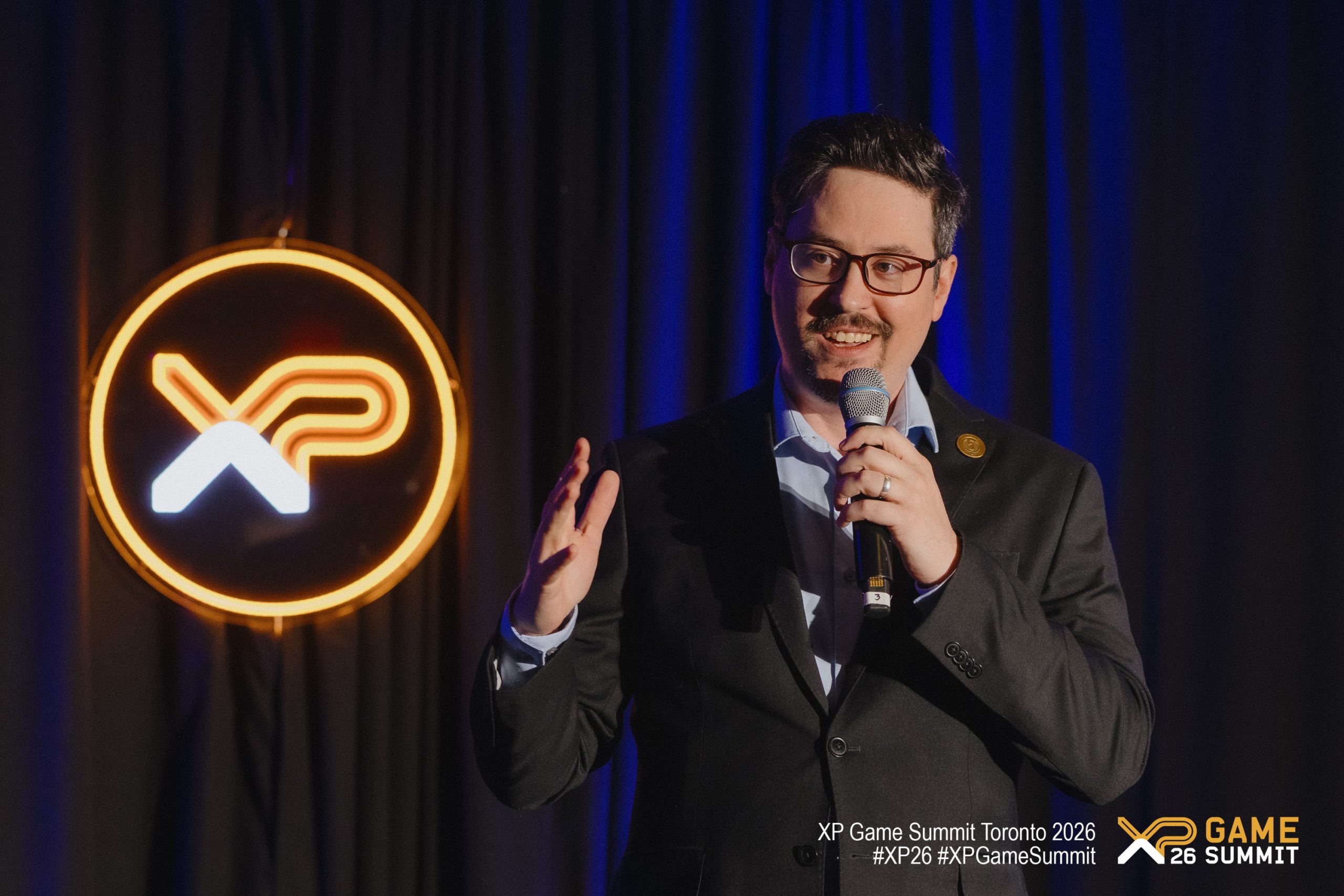 Jason Lepine holding a microphone at the XP Game Summit Toronto 2026, with an 'XP' logo illuminated in the background.
