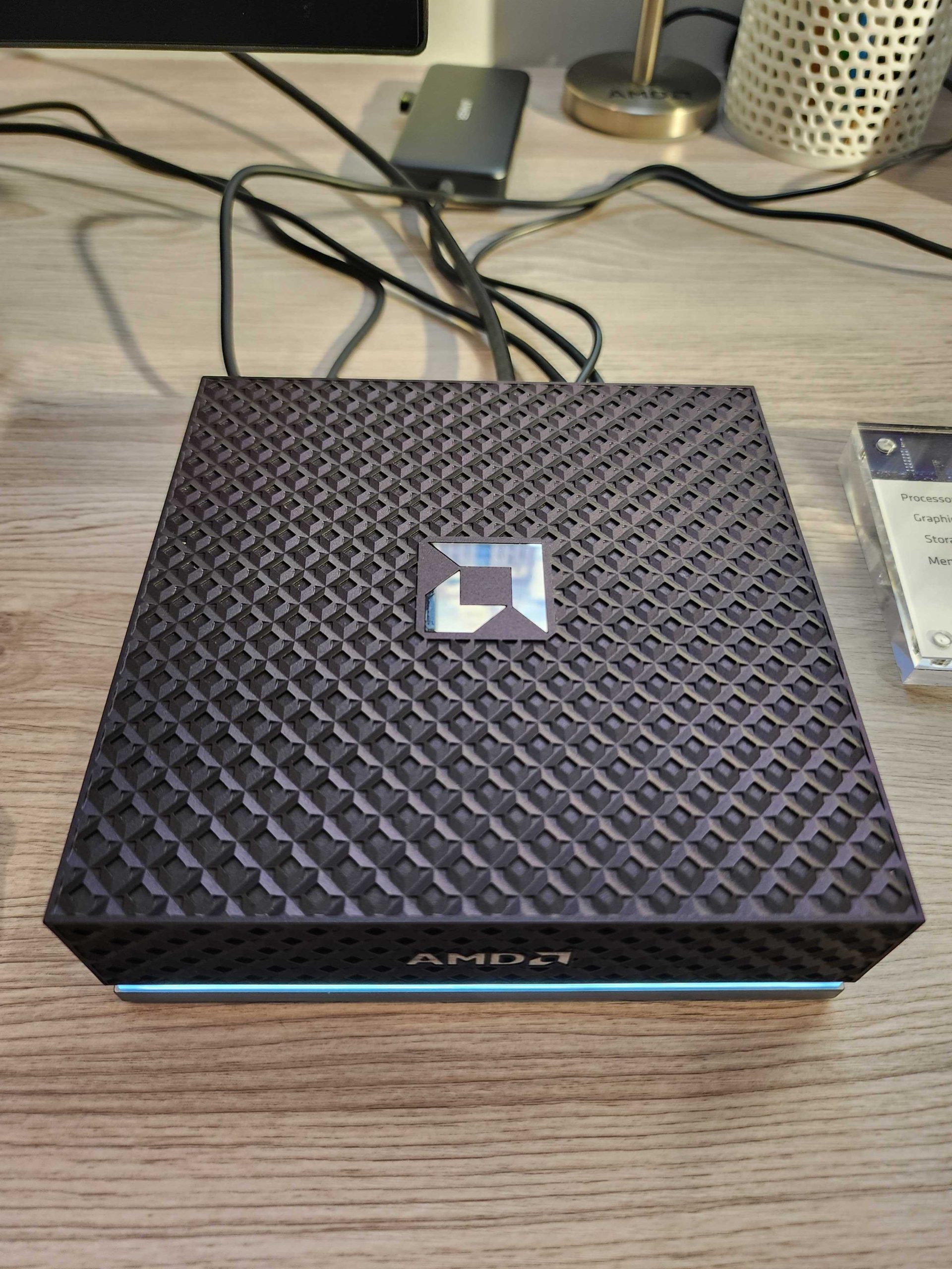 An AMD-branded device with a textured surface is placed on a wooden desk.