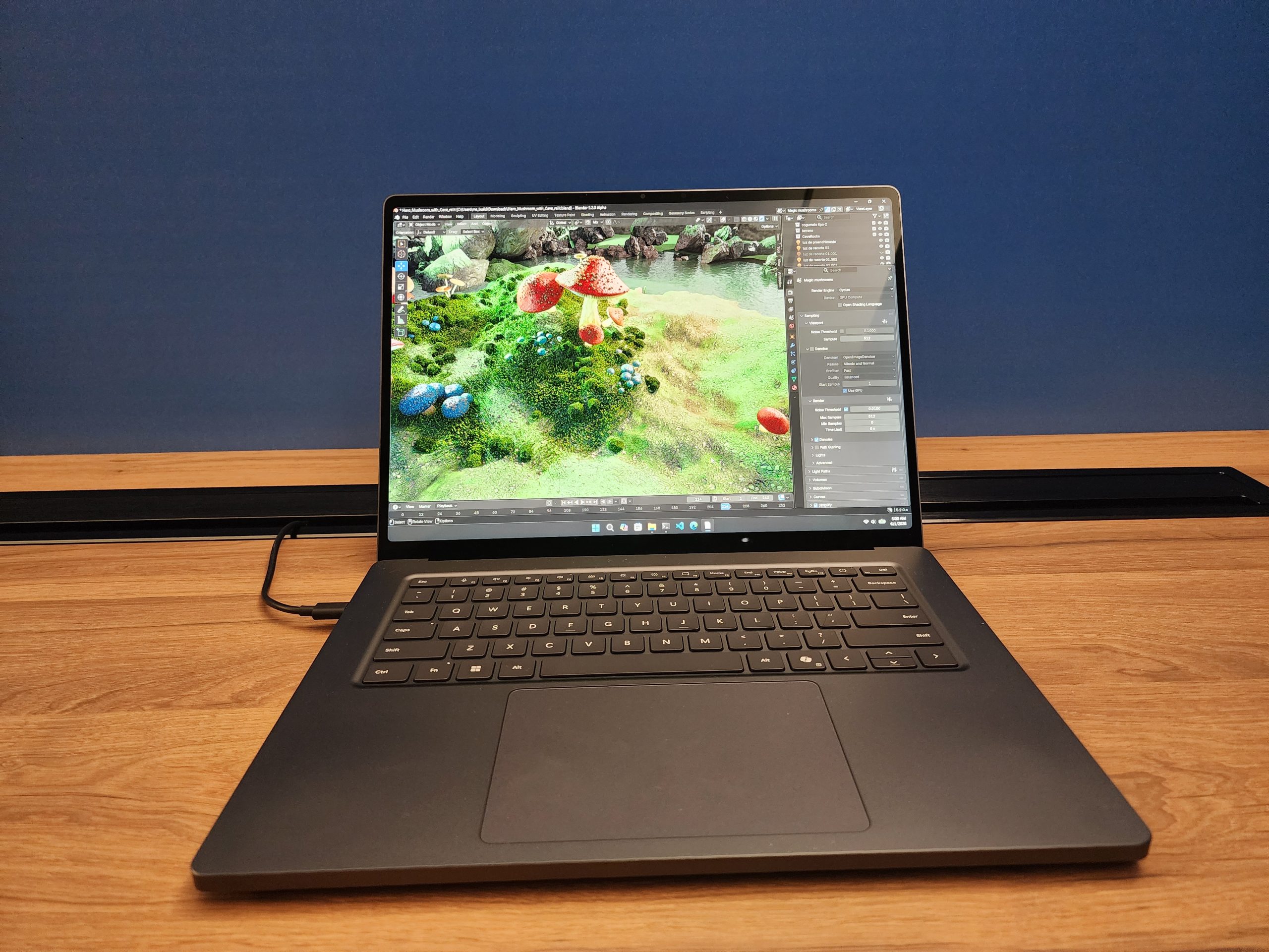 A laptop on a wooden desk displaying 3D design software with a colorful scene featuring mushrooms and foliage.