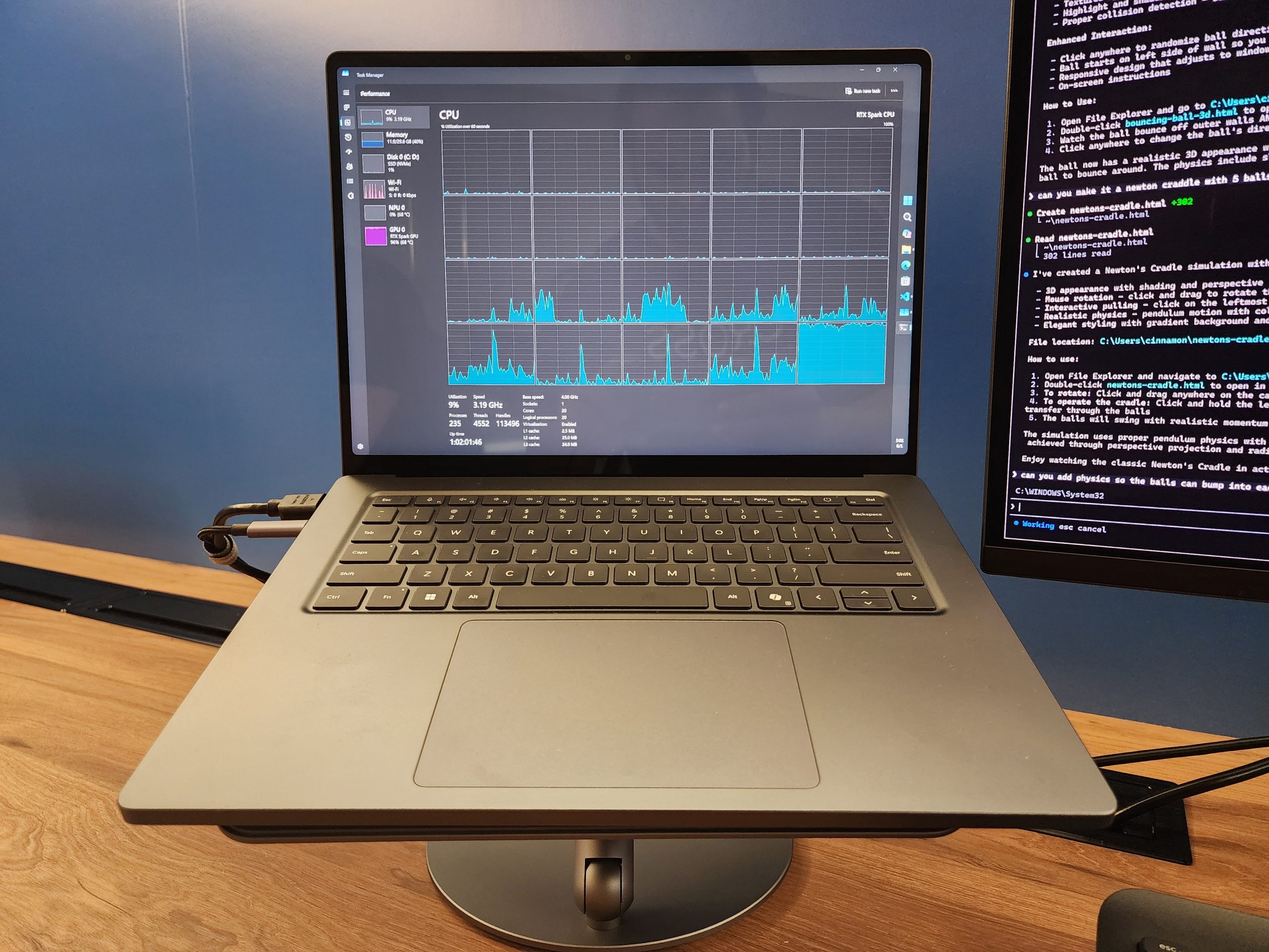 A laptop displaying a performance monitoring tool with CPU usage graphs, next to a monitor showing text code on a wooden desk.