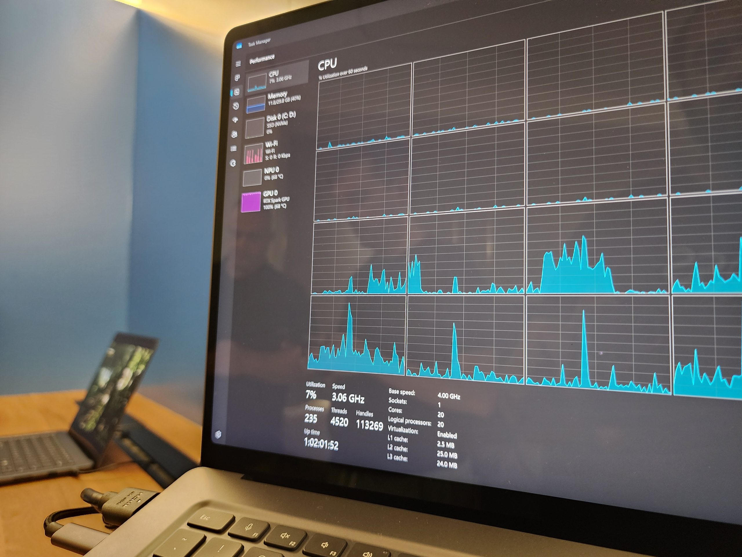 A laptop screen displays the Windows Task Manager's 'Performance' tab showing CPU usage graphs and system specs, with a smaller laptop in the background.