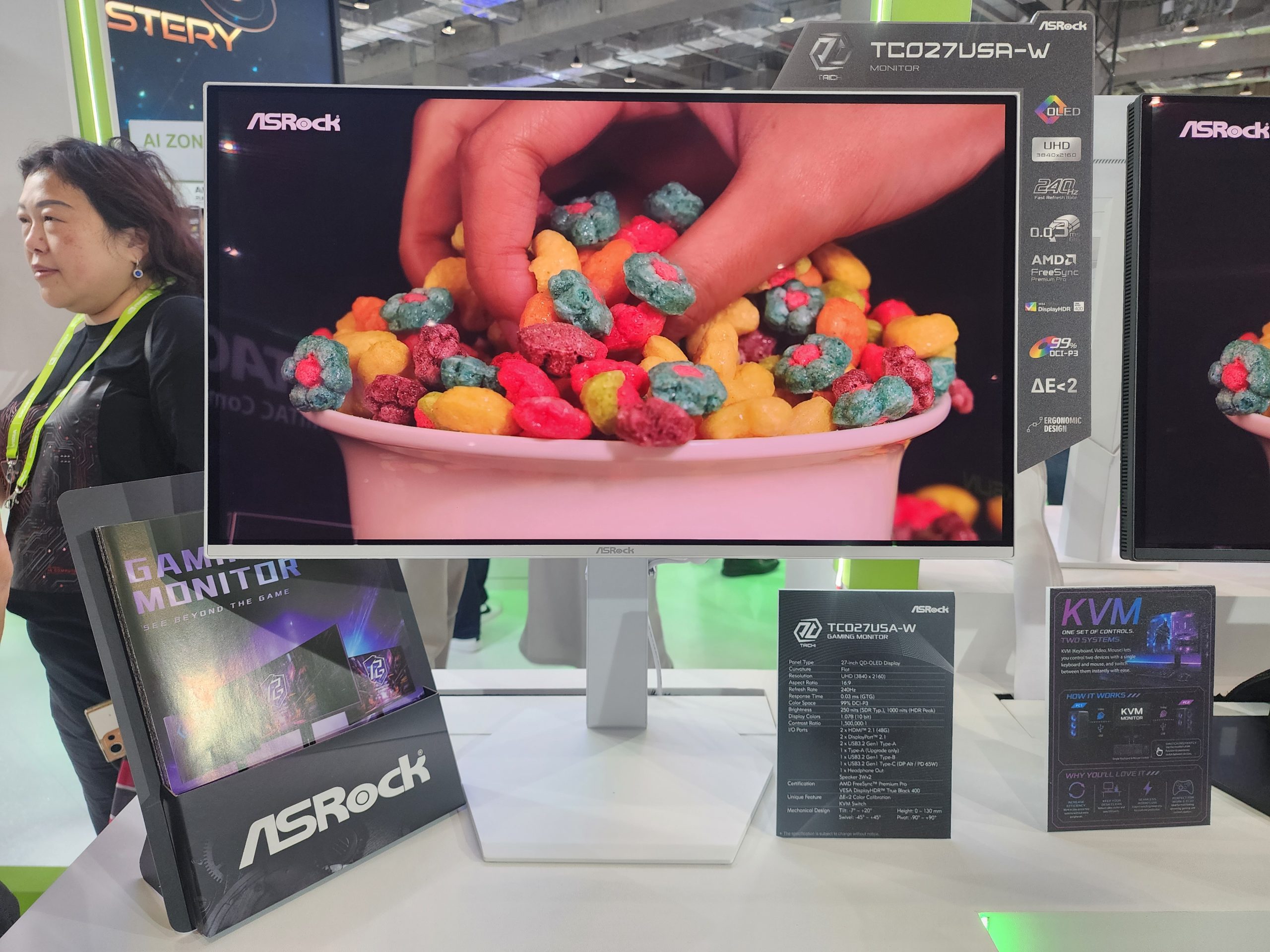 An ASRock TC027USA-W gaming monitor displays a close-up of colorful cereal, with features including '240Hz,' 'UHD,' and 'AMD FreeSync' highlighted on the side panel.