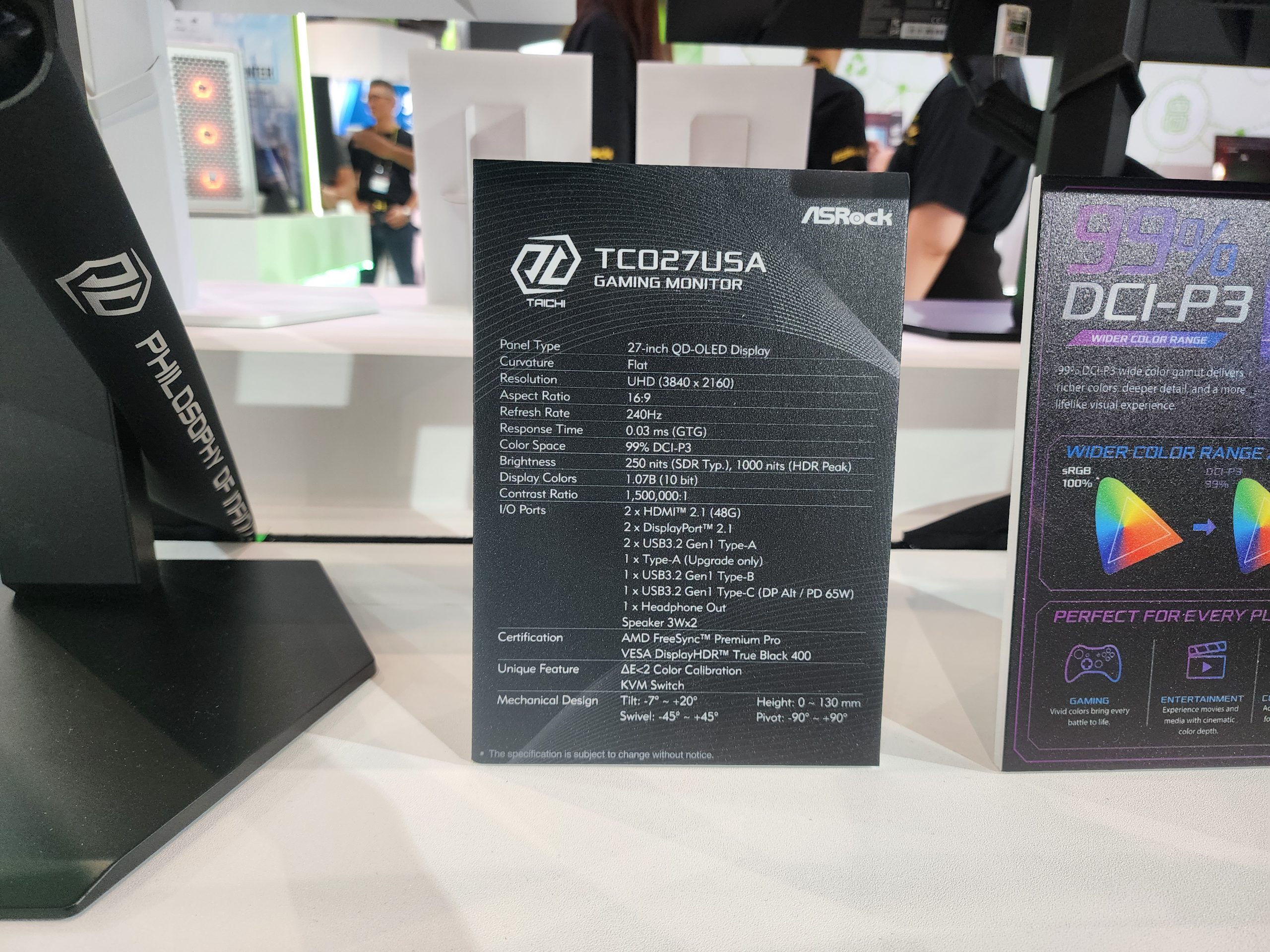 An ASRock promotional display highlights the specs of the TCO27USA gaming monitor, featuring a 27-inch QD-OLED display with a resolution of 3840 x 2160, a refresh rate of 240Hz, and 99% DCI-P3 color gamut coverage.