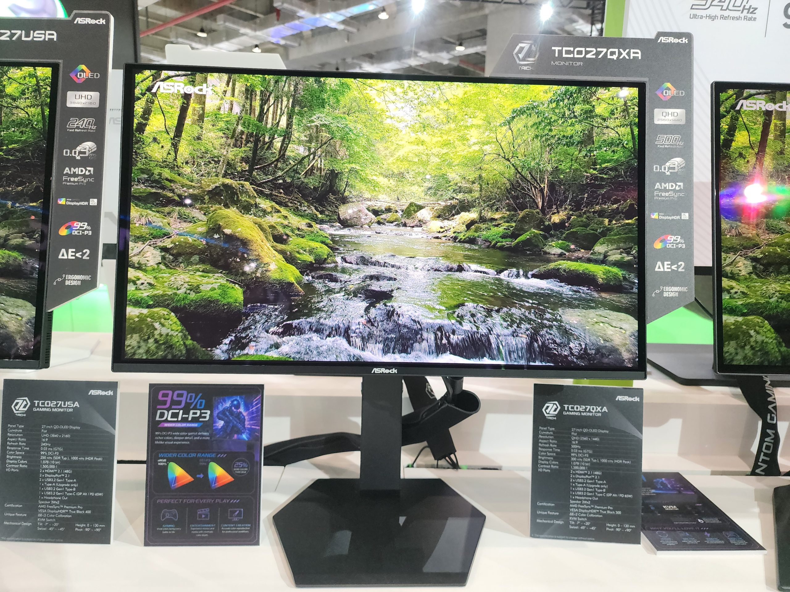 The image shows an ASRock TC027QXA monitor displaying a forest scene, with features including 'QLED,' 'UHD,' '500 nits,' '0.03 ms,' and 'AMD FreeSync.'