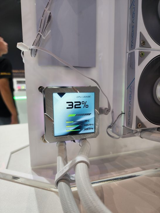 An ASRock Taichi Aqua computer cooling display shows 'CPU Usage: 32%' with additional stats indicating temperature at 28°C, clock speed at 3485 MHz, and fan speed at 3102 RPM.