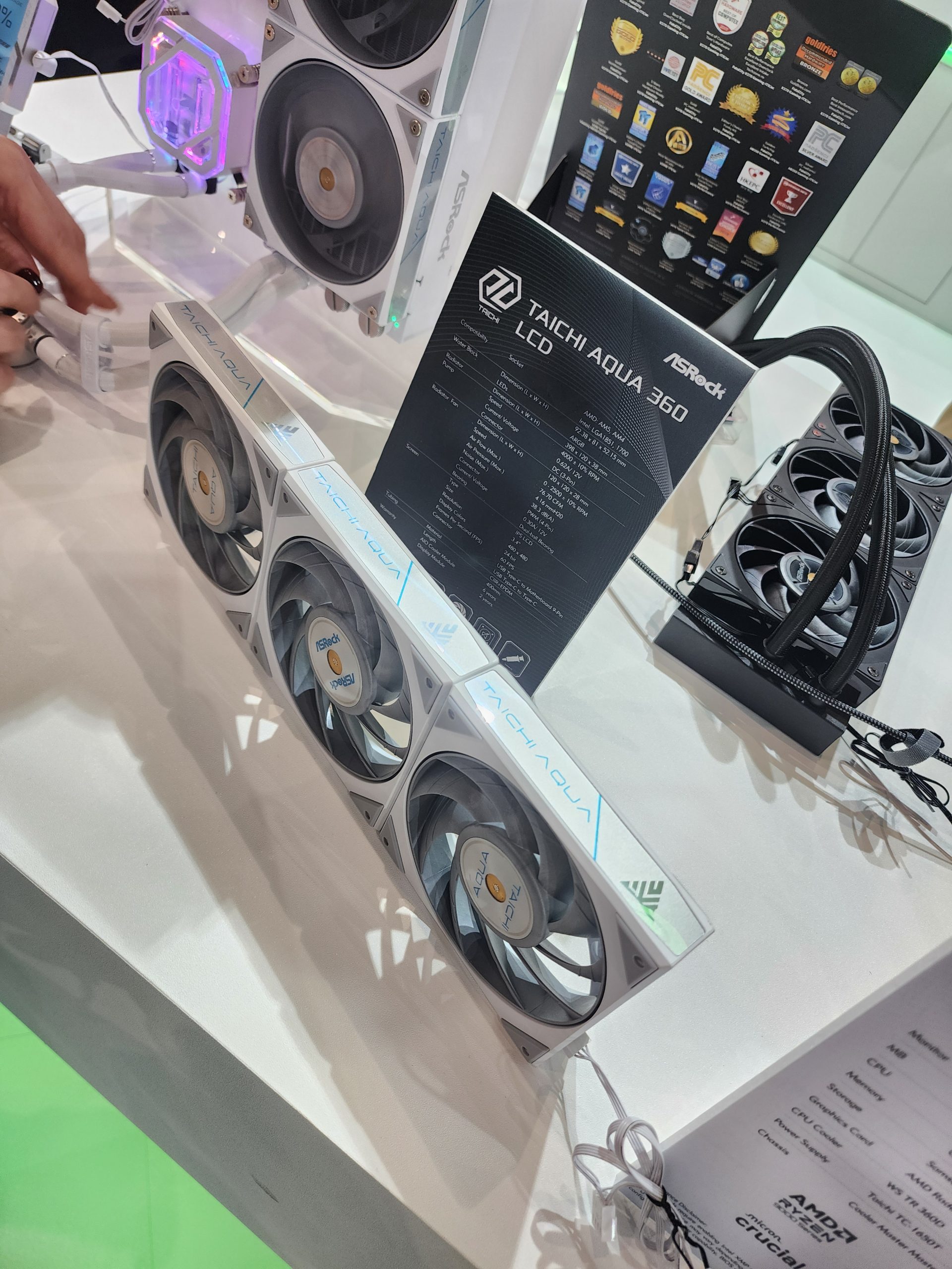 ASRock Taichi Aqua 360 LCD cooling system with visible fans and a detailed specification sheet displayed at a booth.