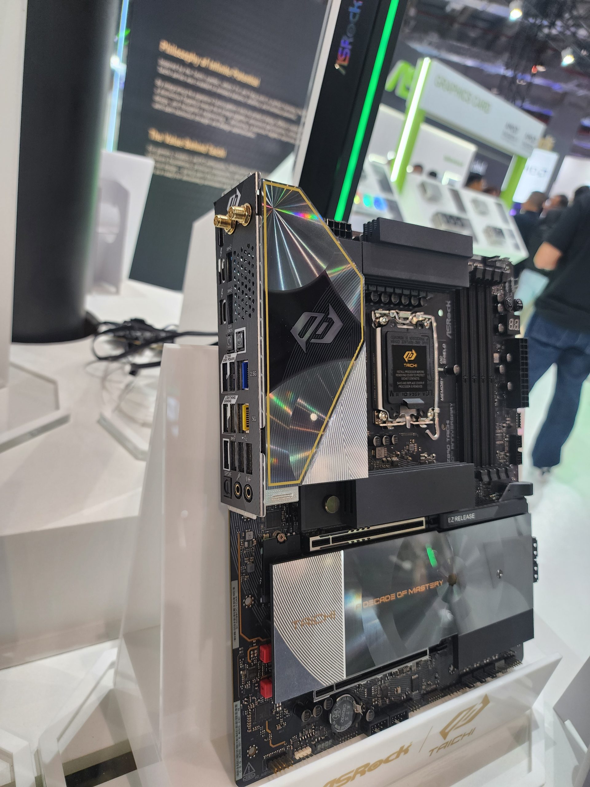 An ASRock Z790 Taichi motherboard is displayed vertically on a stand, featuring design details and logos.