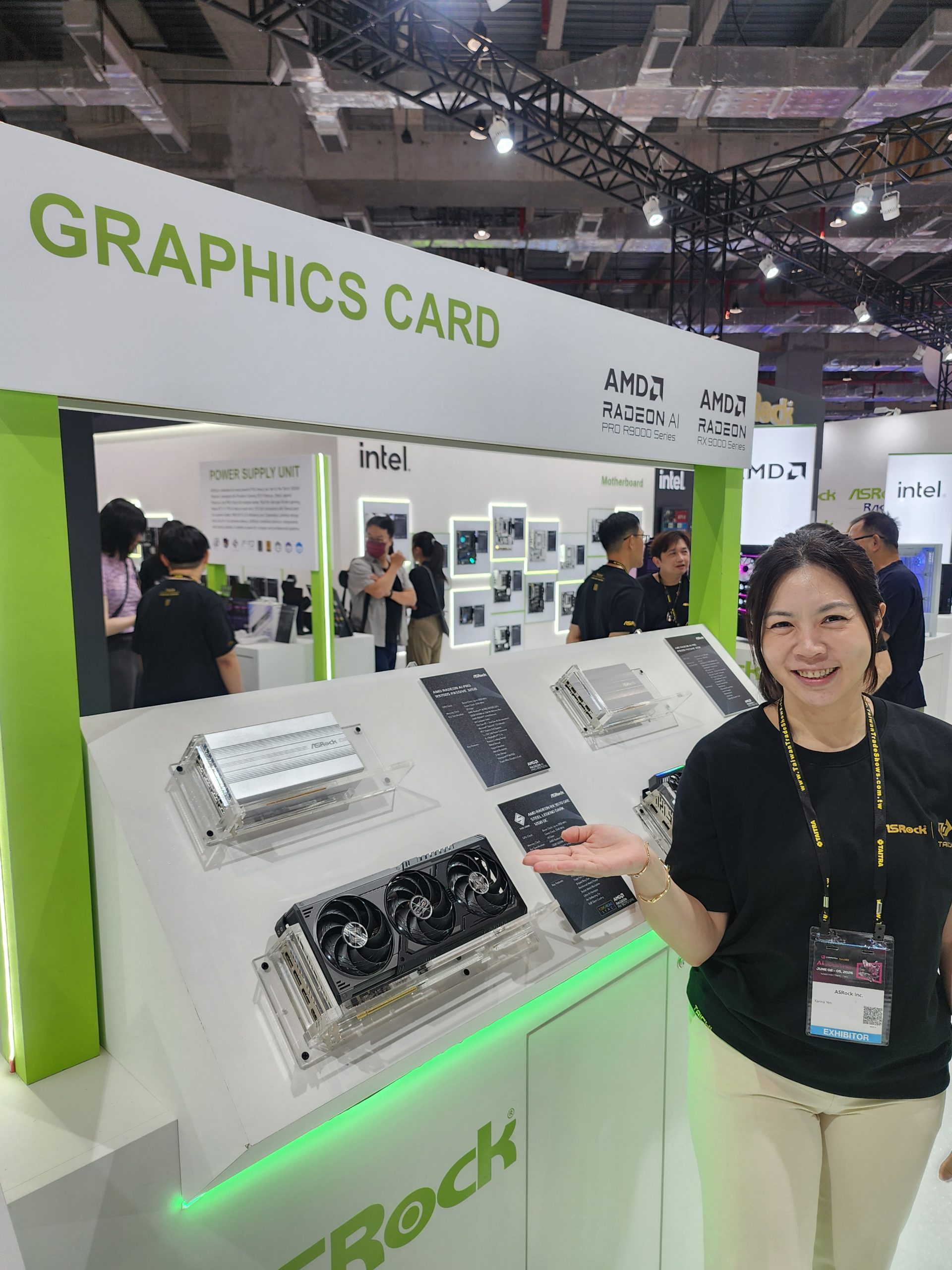 A smiling exhibitor stands beside ASRock graphics cards at a booth displaying the 'AMD Radeon AI Pro 5000 Series' sign at a tech event.