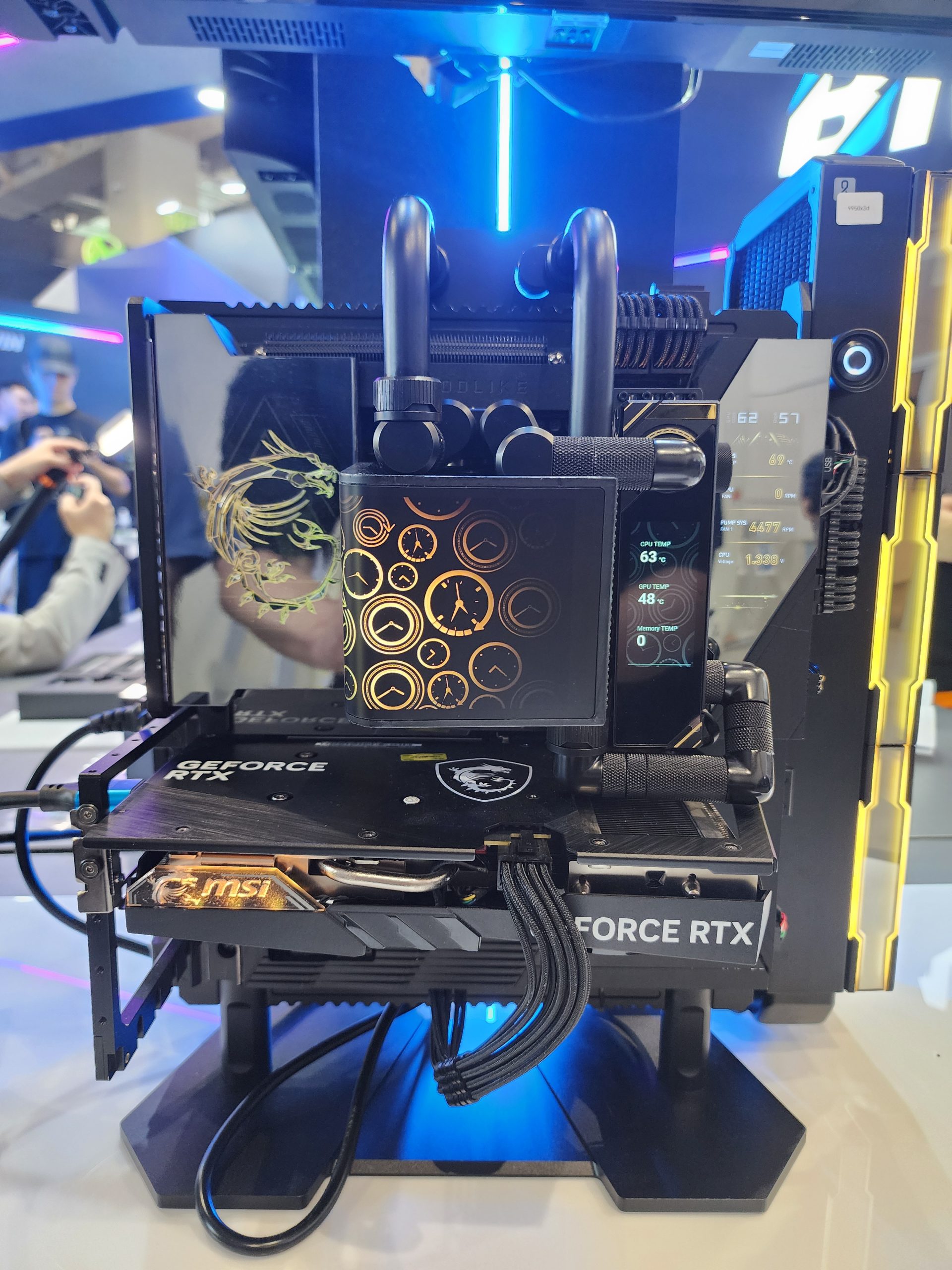 An MSI GeForce RTX graphics card is mounted vertically in a display setup, featuring visible cooling pipes and an electronic display showing diagnostic icons.