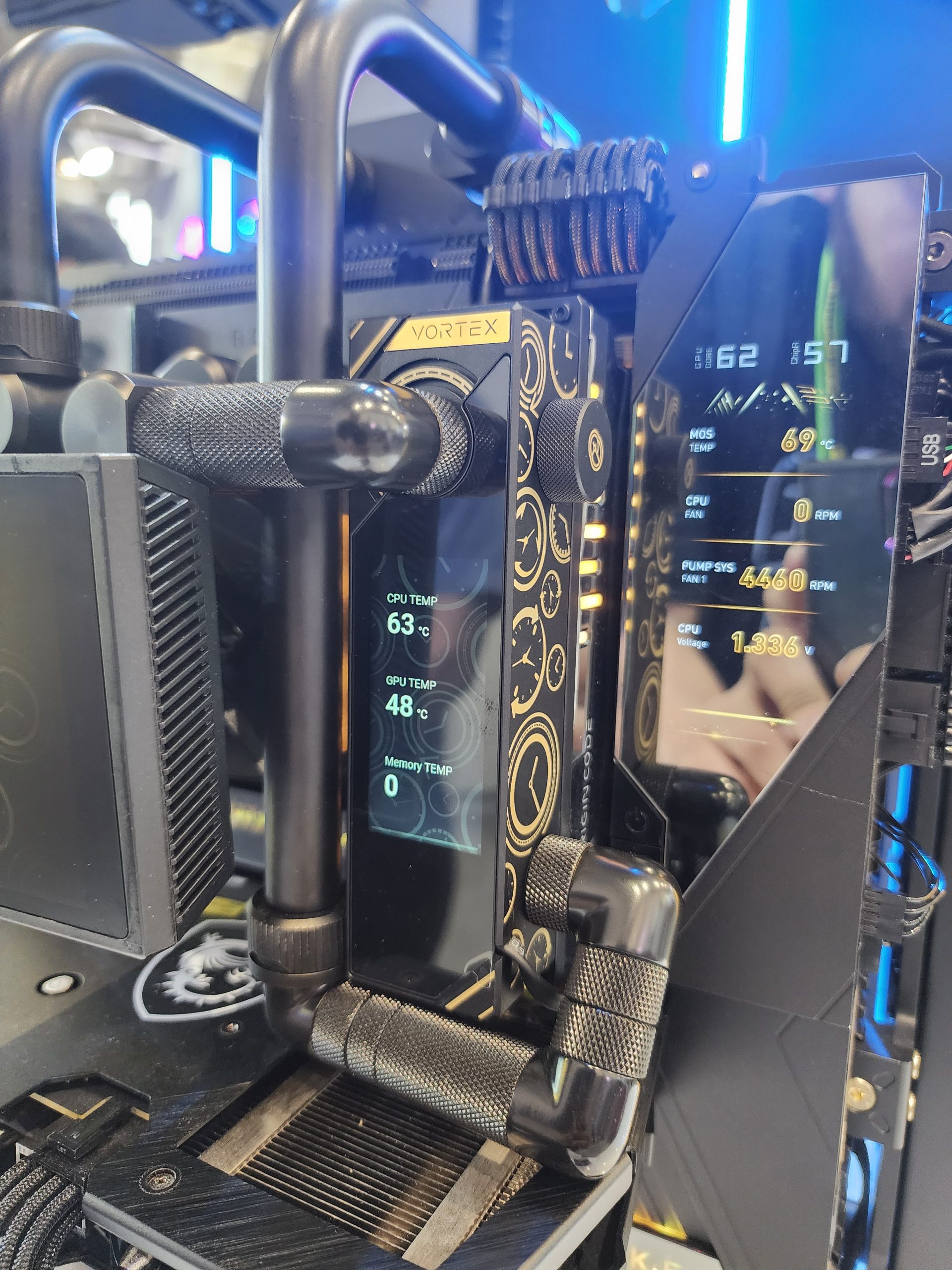 A close-up of a Vortex cooling system display showing 'GPU Temp 63°C' on a black and gold design with visible pipes and hardware details.
