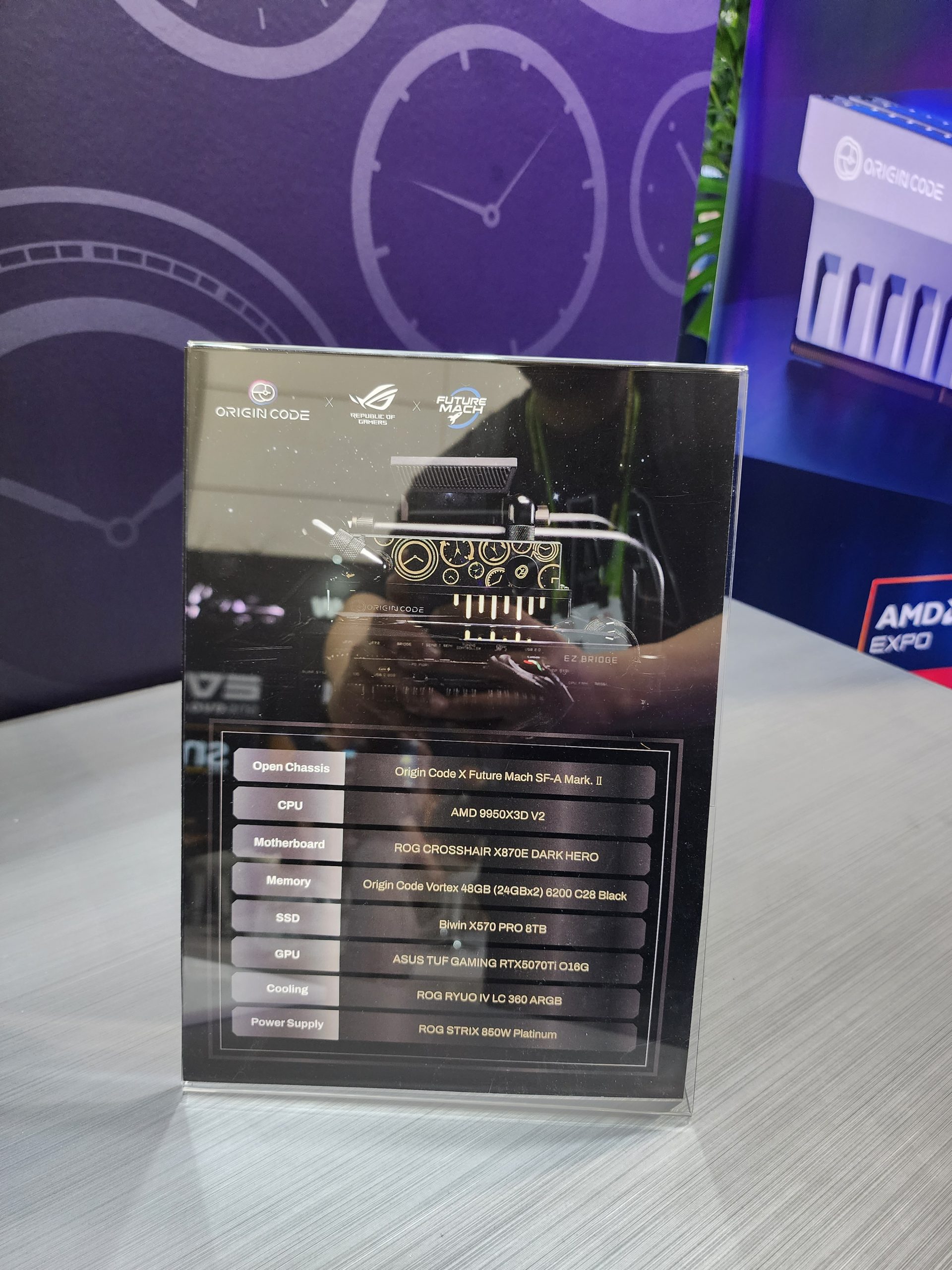 A display features the Origin Code X Future Mach SF-A Mark. II open chassis with an AMD 9950X3D V2 CPU and ASUS TUF GAMING RTX6070TI O16G GPU, alongside other components like the ROG CROSSHAIR X670E DARK HERO motherboard and Origin Code Vortex 48GB memory.