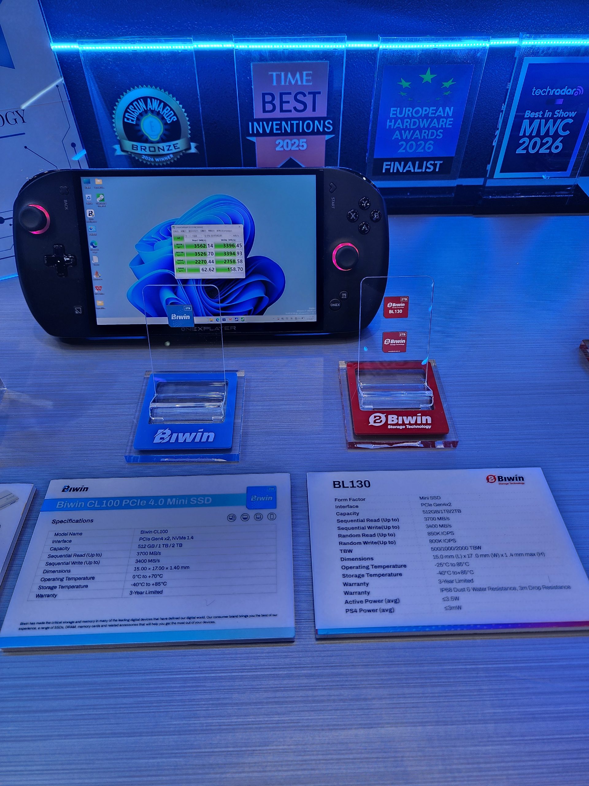 A OneXplayer handheld device displaying a performance test result in front of Biwin CL100 PCIe 4.0 Mini SSD and Biwin BL130 specifications cards, with awards displayed above.