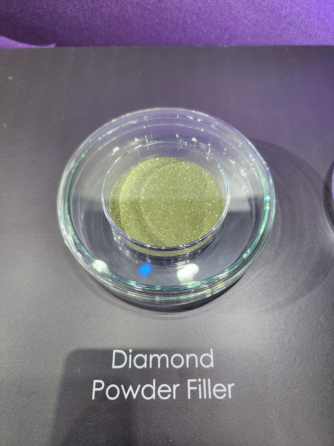 A glass dish containing green Diamond Powder Filler is displayed on a black surface.