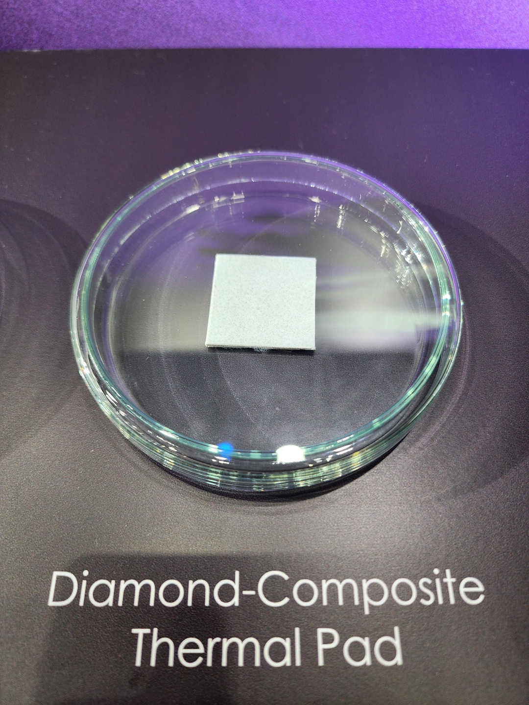A small gray square labeled as a Diamond-Composite Thermal Pad is displayed on a glass dish with a purple background.