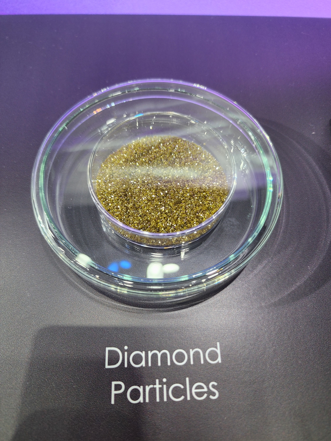 A petri dish containing diamond particles is placed on a surface labeled 'Diamond Particles.'