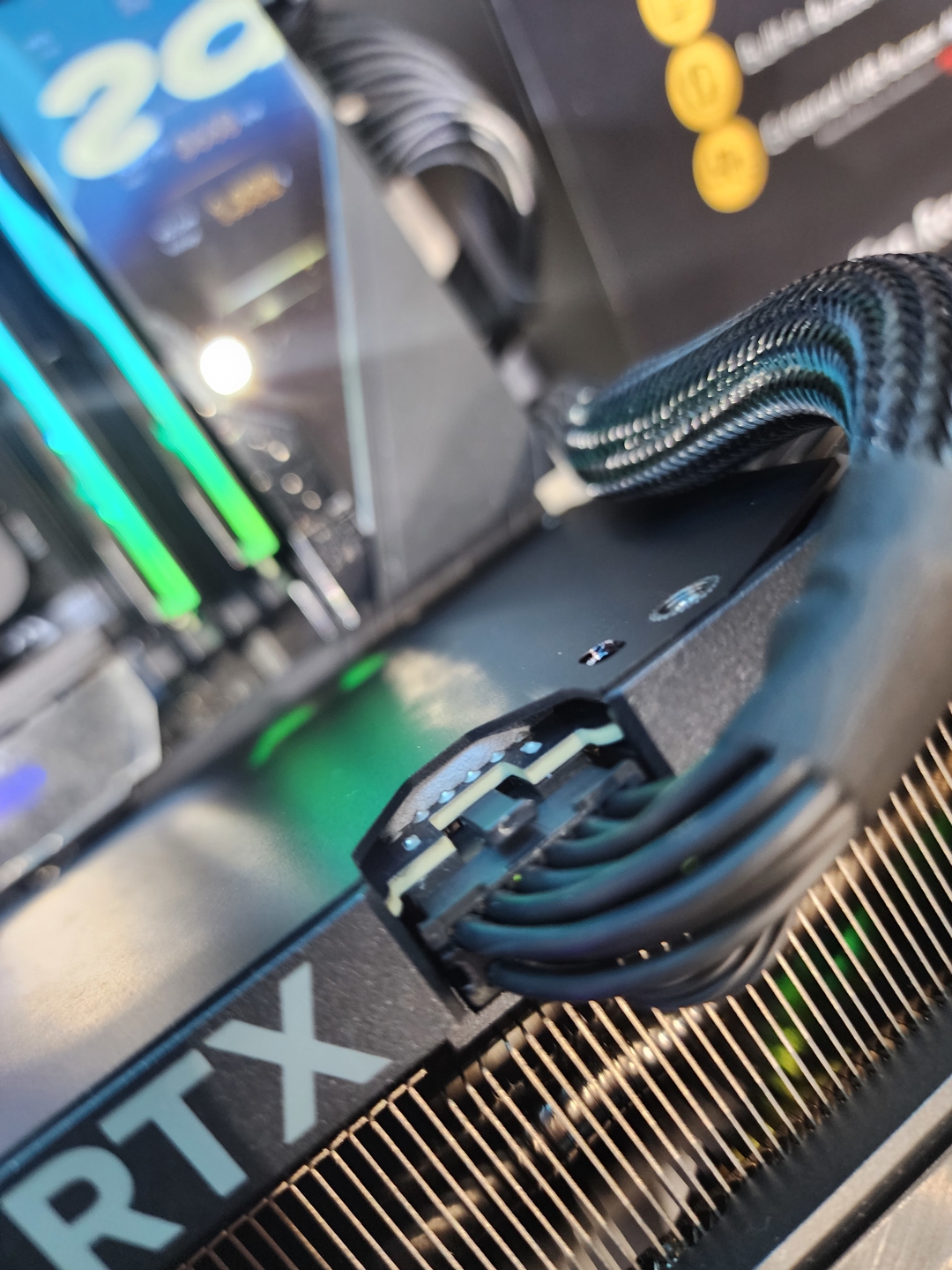 A close-up of an NVIDIA RTX graphics card with a power cable connected, revealing part of its model designation and RGB lighting effects in the background.