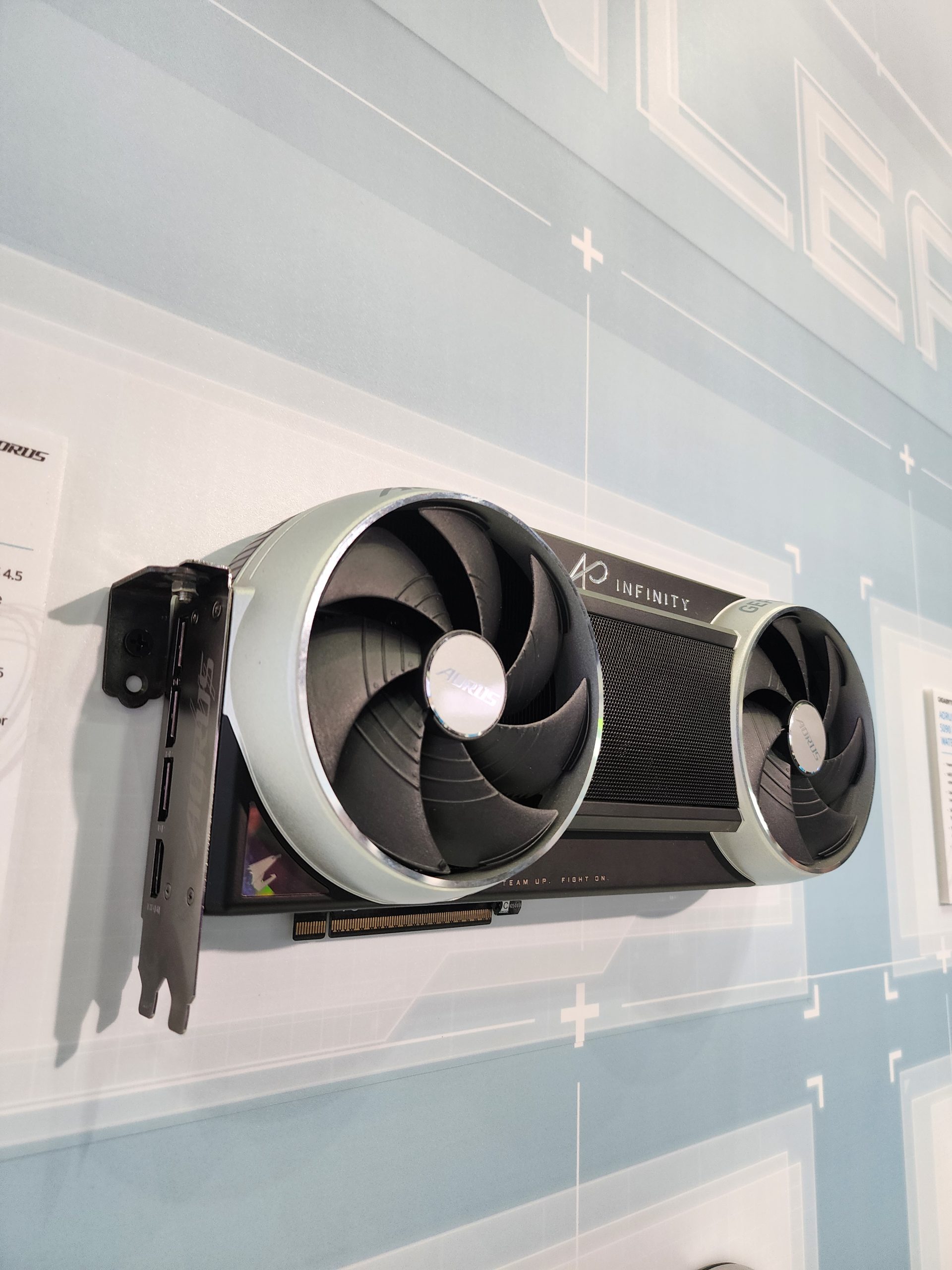 A Gigabyte AORUS graphics card with dual fans labeled 'AORUS' is displayed on a wall, featuring the 'Infinity' branding.