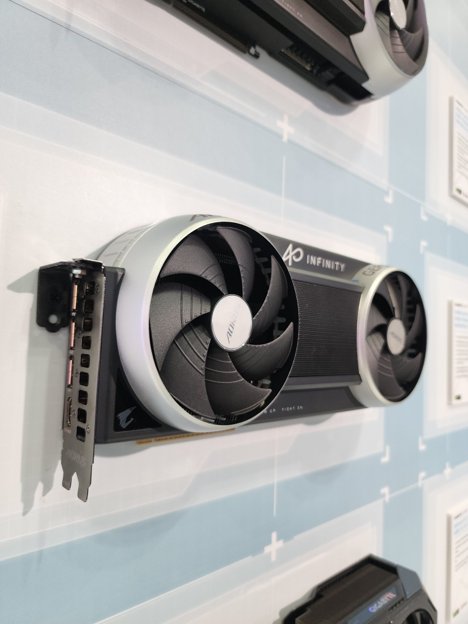 A GIGABYTE AORUS graphics card labeled 'INFINITY' is mounted on a display wall with dual cooling fans visible.