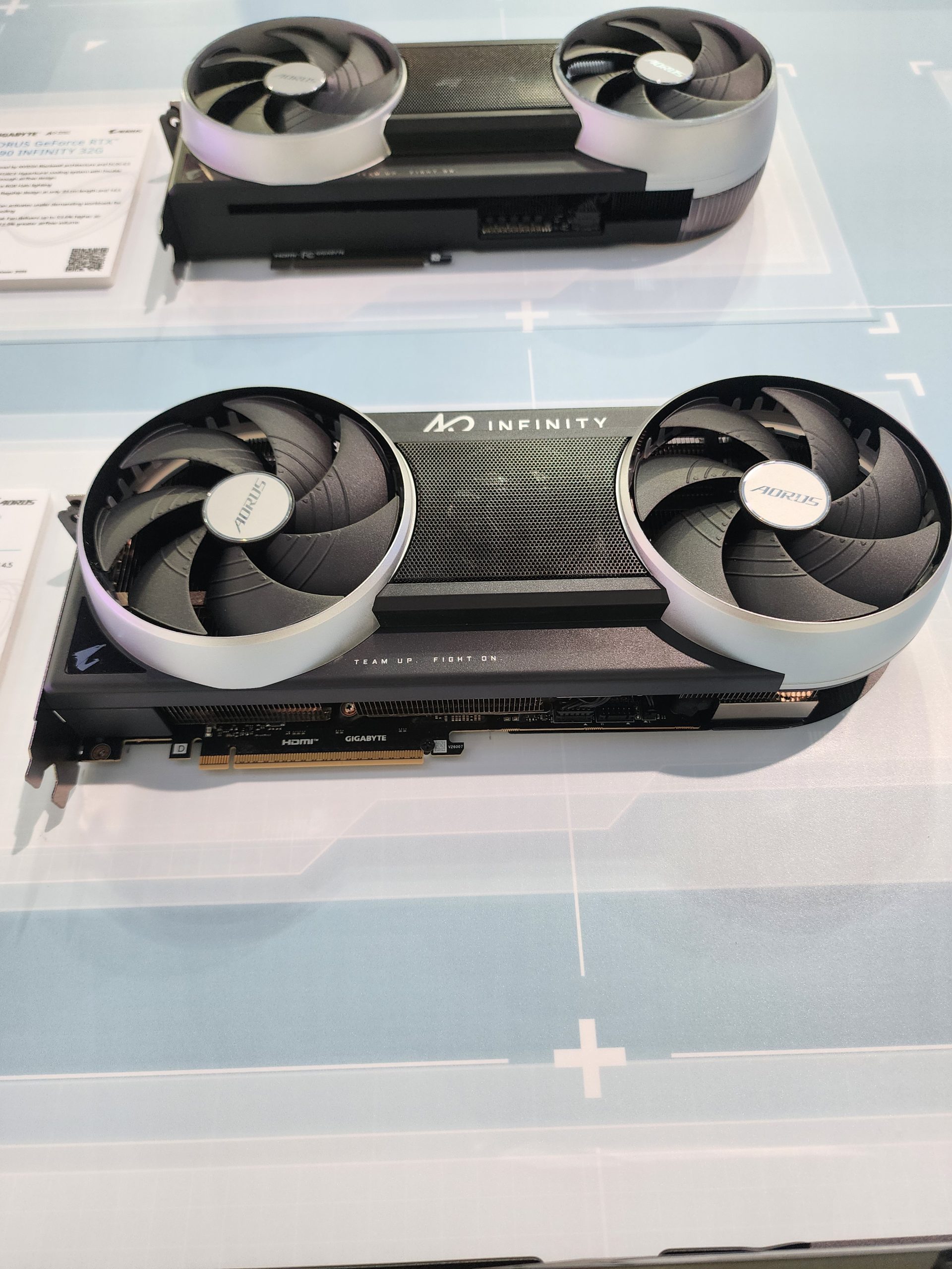 A Gigabyte AORUS GeForce RTX 4090 Infinity 100 graphics card with 'INFINITY' branding displayed on a light blue platform.